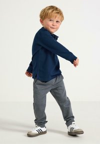 Mørkeblå polo skjorte med lange ærmer og lige bund, parret med grå teksturerede bukser. Hvide sneakers med sorte striber og grå såler.