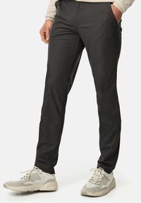 Pantalons noirs ajustés en tissu lisse et extensible, dotés de poches latérales, associés à des chaussures de sport de couleur claire avec un design en mesh.
