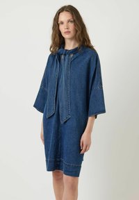 Vestido de mezclilla, azul oscuro, corte relajado, mangas cortas, un lazo en el escote y costura de contraste. Textura suave con un diseño minimalista.