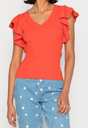 Rotes, geripptes Oberteil mit V-Ausschnitt und frilly Kurzärmeln, kombiniert mit hellblauen Jeans, die weiße Blumenmuster aufweisen.