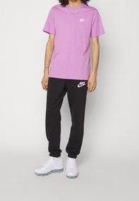 Lila bomullströja med vitt Nike-logotyp, kombinerad med svarta sweatpants som har en vit och rosa Nike-logotyp, samt vita sneakers.