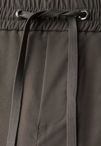 Pantalon gris à cordon de serrage avec une taille froncée, présentant une texture lisse et un léger éclat. Comprend une poche fonctionnelle et des cordons robustes.