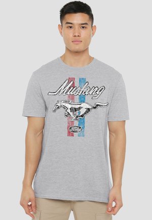 Young man wearing a grey T-shirt with a running horse, "Mustang" text, and red and blue stripes in the background.