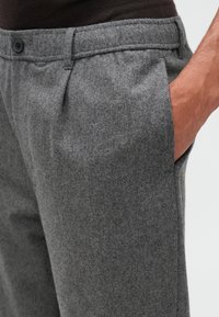 Sive volnene hlače z mešanico vlaken z teksturiranim končnim obdelovanjem, ki vsebujejo stransko žep in gumbasto zapiranje. Slim fit zasnova z krojenim videzom.