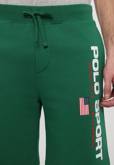 Zelene trenirke z vrvico v pasu, ki imajo rdeče in bele napise "POLO SPORT" ter majhen ameriški zastavni logotip na strani.