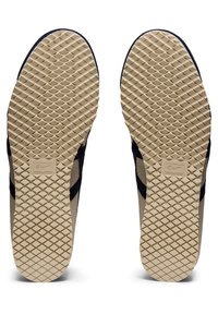 Shoe soles featuring a textured diamond pattern in light tan, edged with dark navy accents along the sides for grip and stability.