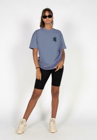 Light blue oversized t-shirt with black graphic on chest, paired with black bike shorts and beige sneakers. Smooth fabric, relaxed fit.