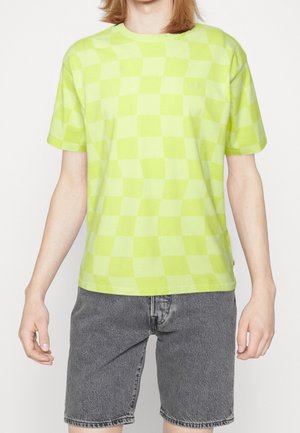 T-shirt à carreaux vert citron en coton, avec des manches courtes et un col rond. Un short en denim gris délavé complète la tenue.