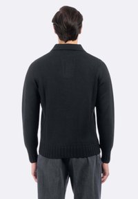 Maglione nero a maglia con orlo e polsini a coste, caratterizzato da un colletto classico e un motivo strutturato. Indossato sopra pantaloni grigio scuro.