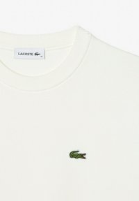 Witte geribde crewneck sweatshirt. Voorzien van een klein groen geborduurd krokodillenlogo op de borst. Gemaakt van zacht, gestructureerd materiaal.