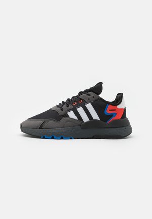 Czarno-szary sneaker z białymi paskami, niebieskimi i czerwonymi akcentami, czarnymi sznurowadłami oraz fakturowaną czarną podeszwą widoczny z boku.