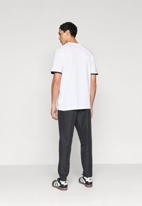 Λευκό T-shirt με μαύρη επένδυση, συνδυασμένο με σκούρο παντελόνι. Το σύνολο διαθέτει casual σχεδιασμό και απαλό ύφασμα, φορεμένο με μαύρα και λευκά αθλητικά παπούτσια.