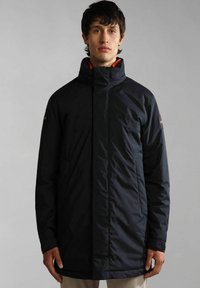 Giacca lunga nera e isolata con colletto alto, texture liscia e tasche laterali. Accentuata da una patch con logo sul maniche sinistro.