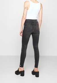 Jeans skinny de tiro alto negros con bolsillos traseros, costuras de contraste y logotipo bordado en el dobladillo. Llevados con tacones de plataforma negros.