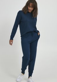 Marineblauwe capuchontrui en jogger set, gemaakt van zachte stof. De hoodie heeft een trekkoord, en de joggers hebben zijzakken en elastische manchetten.
