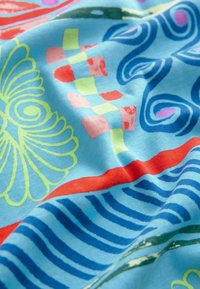Tissu bleu vif avec des motifs abstraits colorés comprenant des spirales jaunes, des blocs à damier rouges et roses, des tourbillons bleu foncé et des rayures rouges et bleues.