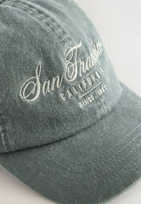 Zöld pamut baseball sapka, a elülső részén fehér hímzett szöveggel: "San Francisco California Since 1983". Ívelt napellenző varrással.