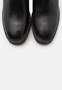 Black leather ankle boots with a rounded toe and slight platform. Smooth texture and minimal stitching detail give a clean appearance.