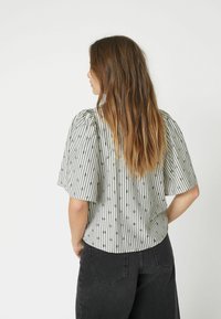 Maglietta a maniche corte di colore grigio chiaro con righe verticali nere e piccoli motivi circolari. Il tessuto sembra liscio e ha una vestibilità comoda.