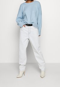 Jasnoniebieski, dzianinowy sweter z opadającymi ramionami, w połączeniu z białymi, wysokimi spodniami dżinsowymi. Białe szpilki i czarny pasek podkreślają całość stroju.