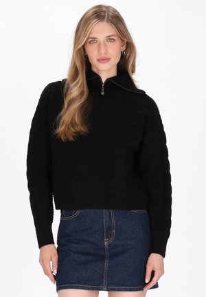Pullover in maglia nera con collo a zip a quarti, maniche lunghe e design cropped, abbinato a una gonna di jeans.