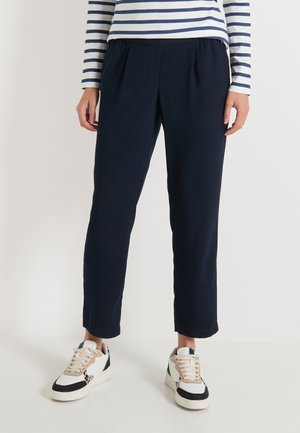 Person wearing navy blue cropped pants, white and black sneakers, and a white long-sleeve shirt with navy blue horizontal stripes.
