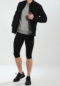 Schwarze Sportjacke mit strukturiertem Finish, grauer Sweatshirt und schwarze, eng anliegende Caprihose. Schwarze Sneaker mit Schnürsenkeln, minimalistisches Design.