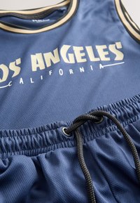 Navy blue mesh tank top with elastic waistband. Features "LOS ANGELES CALIFORNIA" in white lettering and a black drawstring with metal grommets.