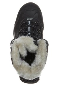 Botas negras aisladas con un exterior sintético. Interior forrado con pelo gris claro para calidez. Cuenta con cordones negros y un logo. Diseño de punta redondeada.