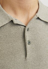 Polo de punto gris claro con un tejido texturizado. Cuenta con un cuello clásico, dos botones y ojales de botón contrastantes.