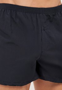 Boxers en coton bleu marine avec une ceinture élastique et un bouton unique à l'avant, présentant une texture lisse et une coupe ample.