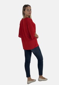 Rode, losvallende top met een gestructureerde afwerking, voorzien van brede mouwen en een ronde halslijn, gecombineerd met donkere skinny jeans en lichte flats.