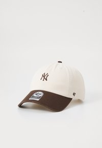 Beige katoenen baseballpet met een bruine klep, voorzien van een geborduurd NY-logo in bruin en een zwart-witte merklabel aan de voorkant.