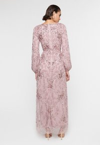 Vestido largo y rosa con mangas largas, que presenta intrincados bordados y patrones florales. Superposiciones de tela transparente con una cintura ajustada y cierre de cremallera.
