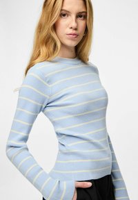 Gaiši zils ribotais trikotāžas džemperis ar horizontālām dzeltenām svītrām, apaļu kakla izgriezumu un garām piedurknēm. Raksturota pieguļošs siluets un sānu kabatas.