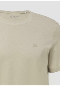 Jasno beżowy t-shirt z krótkim rękawem, okrągłym dekoltem, delikatnym logo na klatce piersiowej oraz nadrukowaną marką "s.Oliver" wewnątrz kołnierzyka.