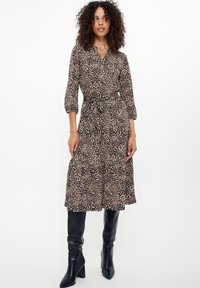 Schwarzes Kleid mit leicht gesprenkeltem Muster, geknöpftem Kragen, Dreiviertelärmeln, Bindegürtel und gestuftem Rock, kombiniert mit knielangen schwarzen Stiefeln.