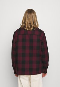 Chemise en flanelle à carreaux bourgogne et noire, dotée de manches longues, de poignets à boutons et d'un ourlet droit. Tissu doux avec une coupe décontractée.