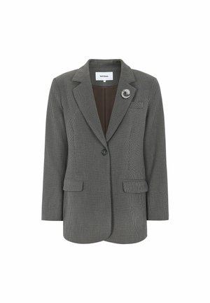 Szürke kockás blézer, amely testre szabott szabású, visszahajtott gallérral, egygombos záródással, két elülső zsebbel, és egy díszcsattal a bal oldalon.