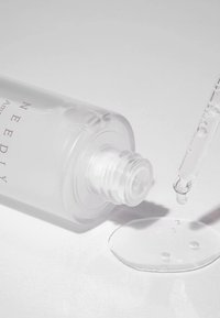 Clear glass dropper bottle with a white label, containing a viscous, transparent serum. A dropper is poised above a droplet on a flat surface.