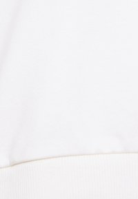 Bílá bavlněná mikinová látka s hladkou texturou a žebrovaným lemem. Žádné viditelné vzory nebo motivy. Čistý a minimalistický vzhled.