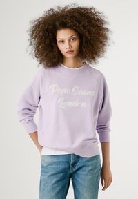 Svetlofialová mikina s nápisom "Pepe Jeans London" v bielej farbe, voľný strih a rebrované manžety. Skombinovaná s modrými džínsy.