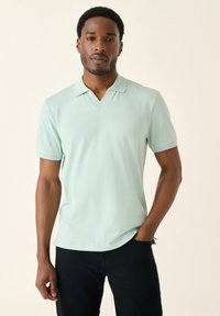 Polo de manga corta en verde claro con dise�ño de cuello en V, que presenta una textura suave y un ajuste relajado, combinado con pantalones negros.