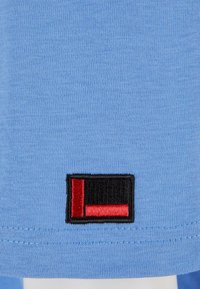 Tricou de culoare albastru deschis, realizat din bumbac texturat, cu un logo brodat în negru și roșu la margine. Design cu mâneci scurte.