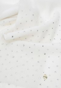 Tessuto bianco con una texture a coste, decorato con perline argentate sparse. Presenta un'etichetta dorata "GUESS", che aggiunge dettaglio al design.