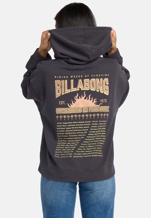 Felpa con cappuccio nera con un grande logo "BILLABONG" e una grafica solare sulla schiena, accompagnata da testi che descrivono varie località di surf.