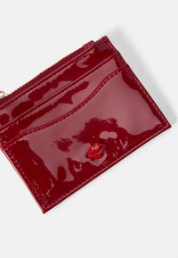 Czerwony portfel z lakierowanej sztucznej skóry o błyszczącym wykończeniu, z kieszenią na zamek i 3D akcentem w kształcie ust z przodu. Gładka tekstura i elegancki design.