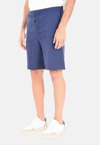 Bermuda in cotone blu navy con cintura elastica e cordoncino. Presenta tasche laterali e una vestibilità comoda, abbinata a sneakers bianche.