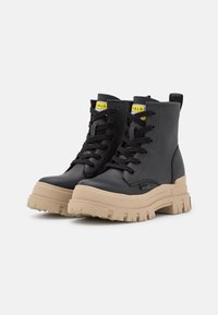 Bottines noires en cuir texturé, avec des lacets noirs, une semelle beige épaisse et des accents de logo en jaune.