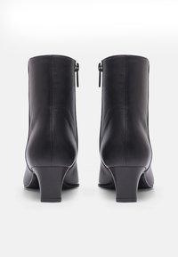 Bottes noires à la cheville en cuir lisse, présentant un talon bloc de hauteur moyenne et des zips sur les côtés. Design simple avec une silhouette épurée.
